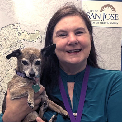 Photo of Kiska standing in front of a map of San Jose holding a senior chihuahua
